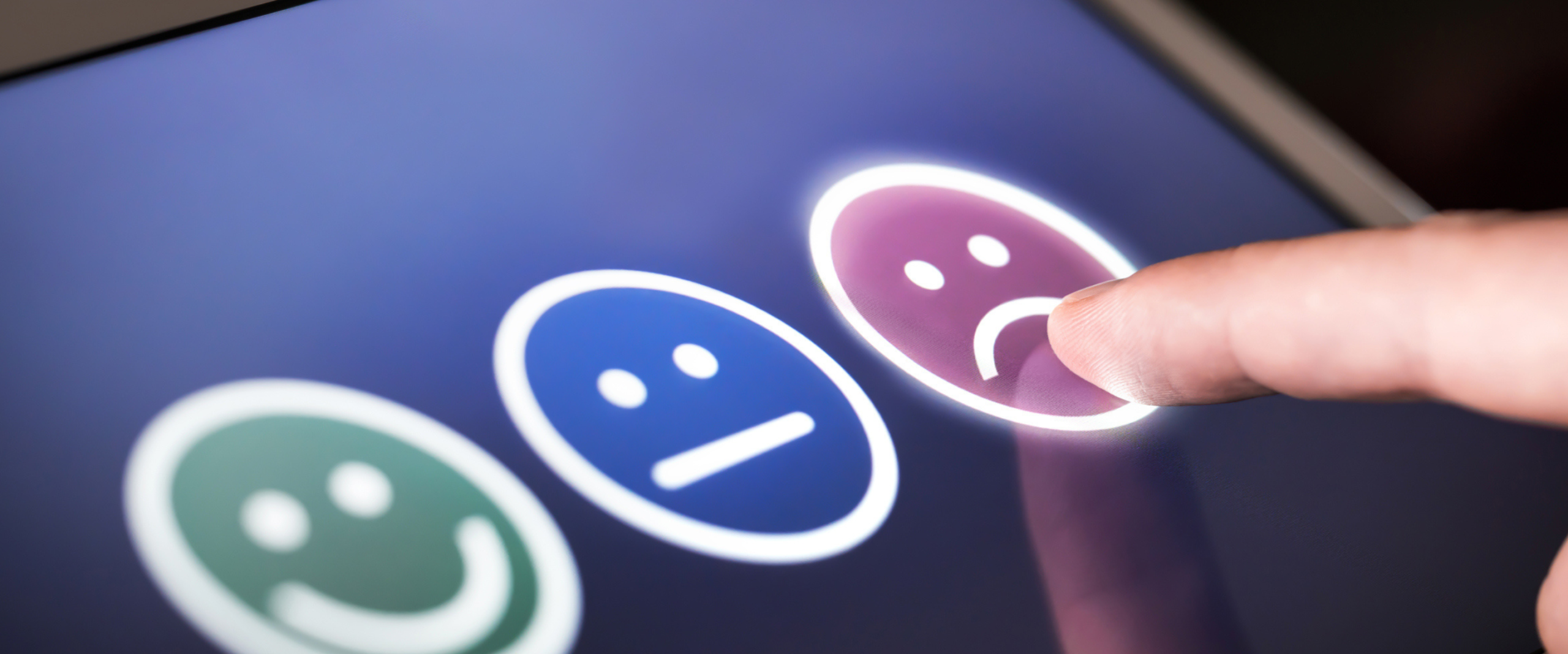 Finger pointing to a purple frowny face icon on a dark blue digital screen.