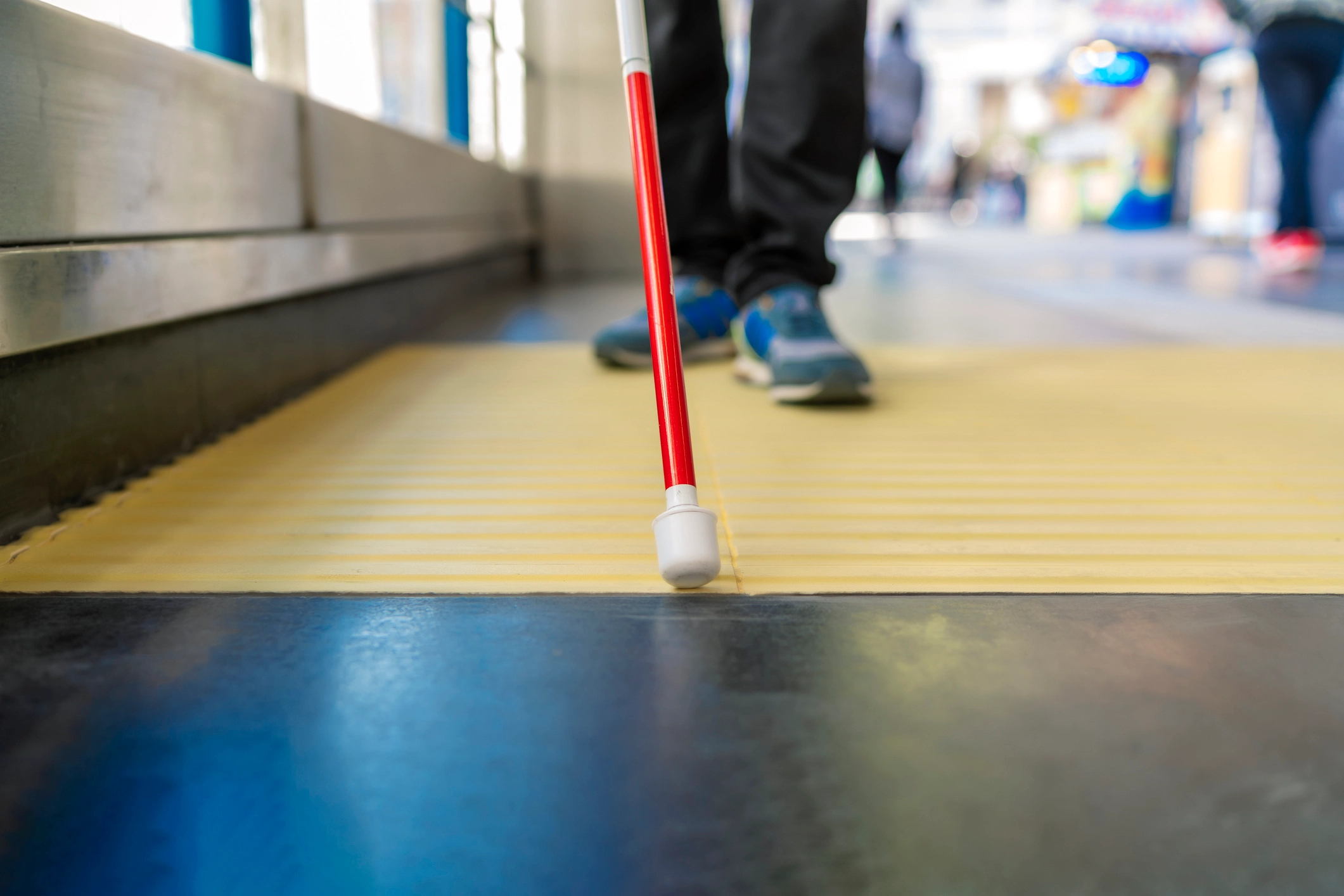 Legs and feet of blind person using his red cane to guide himself down the street.