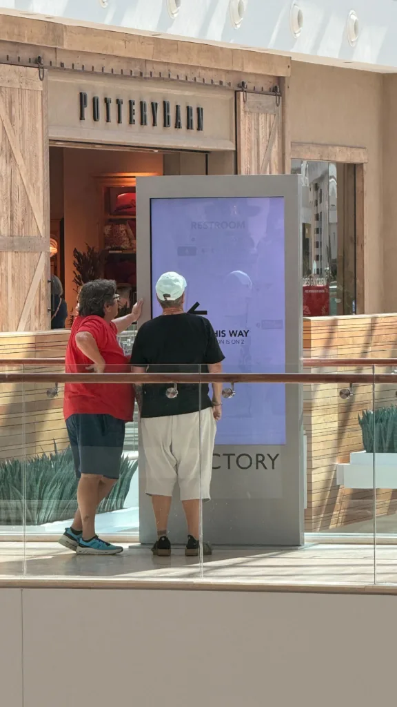 man and woman interacting with digital kiosk during the daytime on second level of shopping mall.