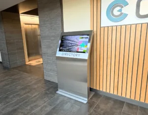 Standalone interactive digital kiosk in medical office lobby helping patient experience finding doctors and suites.