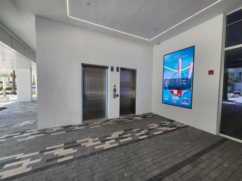 bright blue digital touchscreen directory in an elevator bank wall in commercial office building.